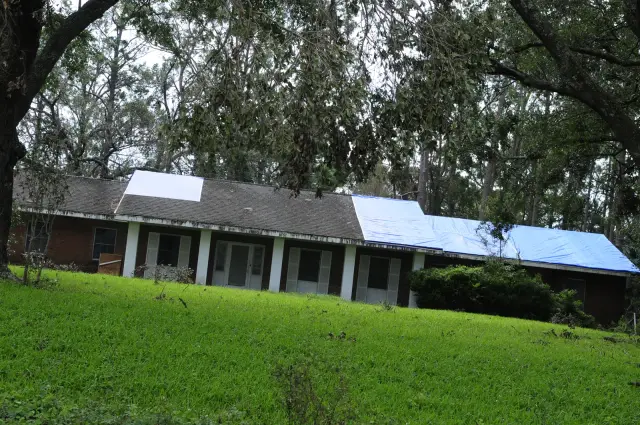 Residential home with full blue emergency tarp installed across the roof to prevent further water damage