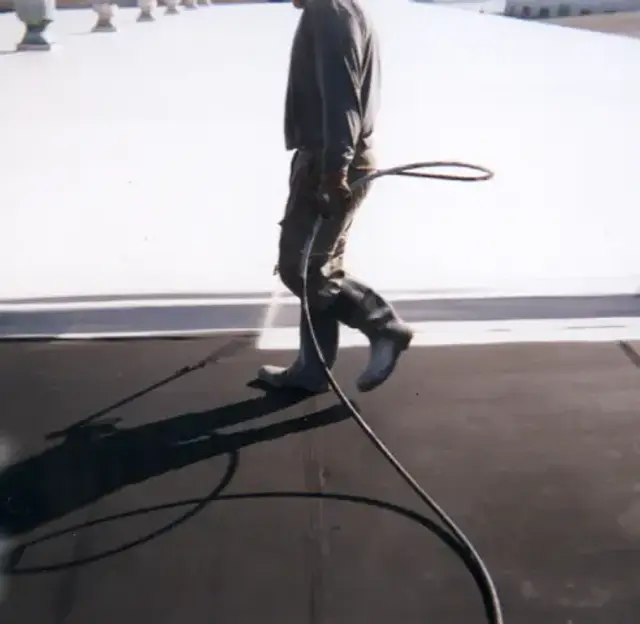 Commercial flat roof being top-coated with white elastomeric roof coating using a roller