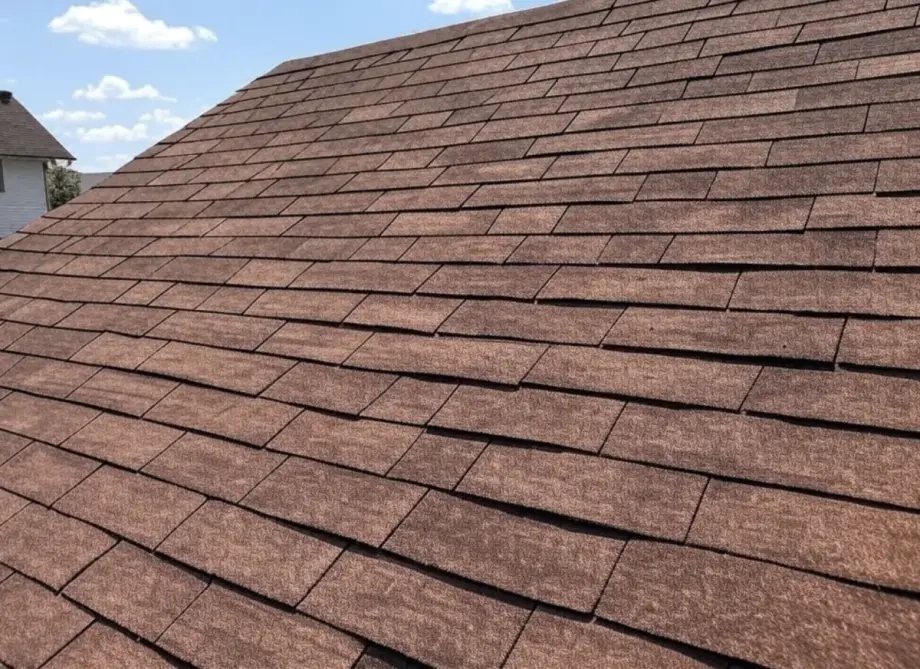 Close-up of brown architectural asphalt shingle roof on a residential home against a clear blue sky