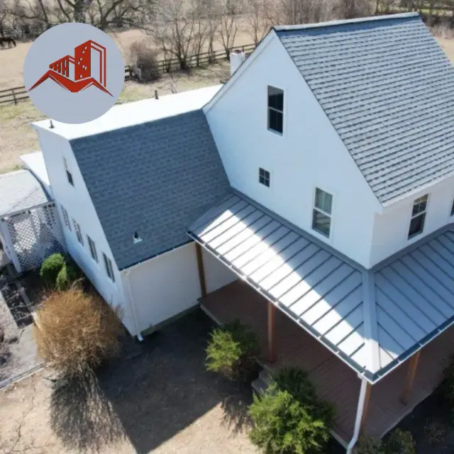 Aerial drone view of a white two-story farmhouse with gray asphalt shingle main roof and standing seam metal porch roof