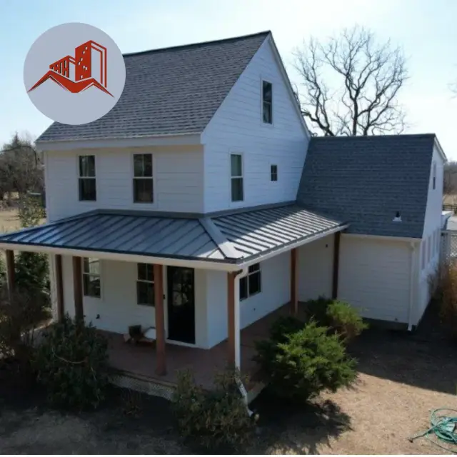 Aerial view of a white farmhouse with charcoal asphalt shingle roof and dark standing seam metal wraparound porch