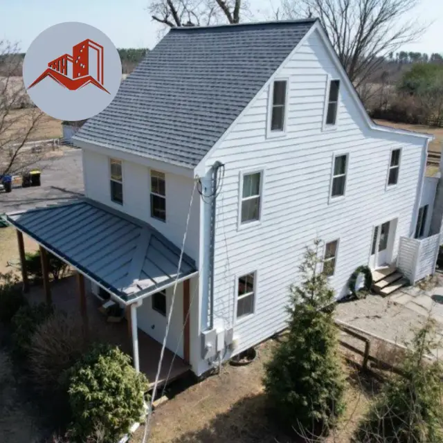 Aerial drone shot of a tall white farmhouse with gray asphalt shingle main roof and dark metal porch roof