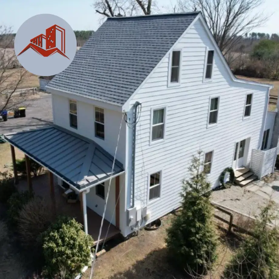 Aerial drone shot of a tall white farmhouse with gray asphalt shingle main roof and dark metal porch roof