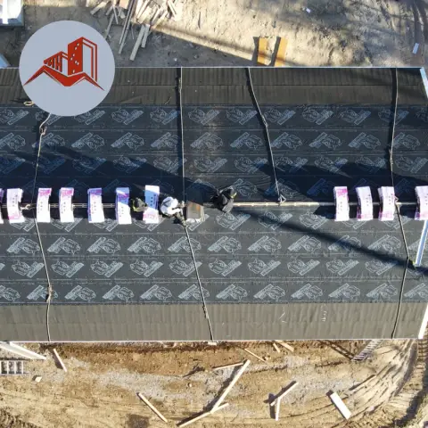 Aerial view of a large commercial flat-pitch roof being installed with synthetic underlayment