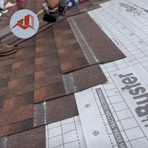 Brown asphalt shingles being installed over white synthetic underlayment with a nail gun