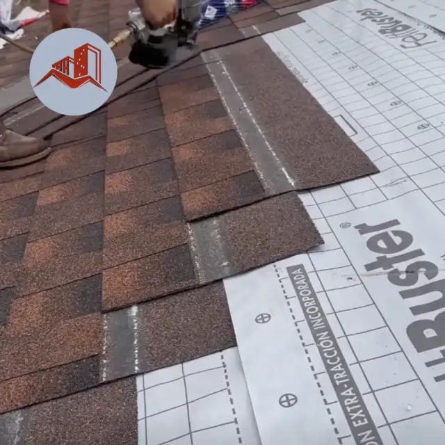 Brown asphalt shingles being installed over white synthetic underlayment with a nail gun visible at top