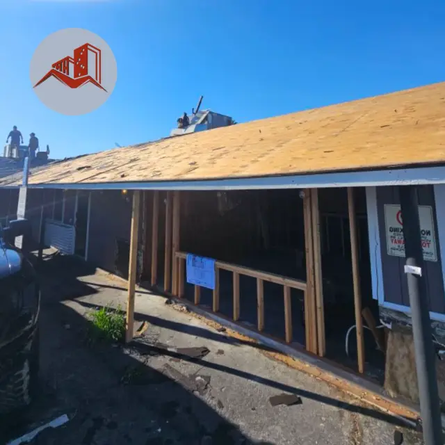 Roof tear-off in progress with plywood decking exposed and crew visible at the far end of the roof