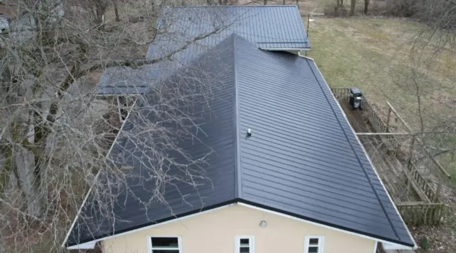 Aerial drone view of a dark gray standing seam metal roof on a single-story home with stucco siding