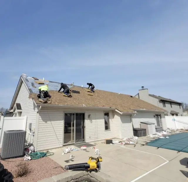 Three roofers installing dimensional asphalt shingles on a single-story suburban home with white siding