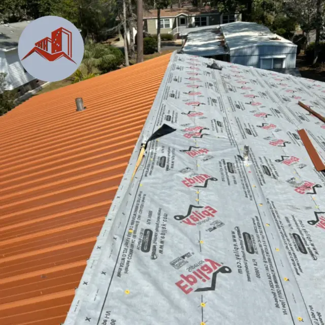Orange ribbed metal roofing panels being installed over synthetic underlayment on a residential home