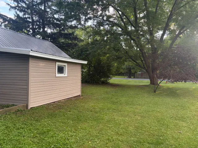 Side view of a detached garage with new tan vinyl siding and gray ribbed metal roof
