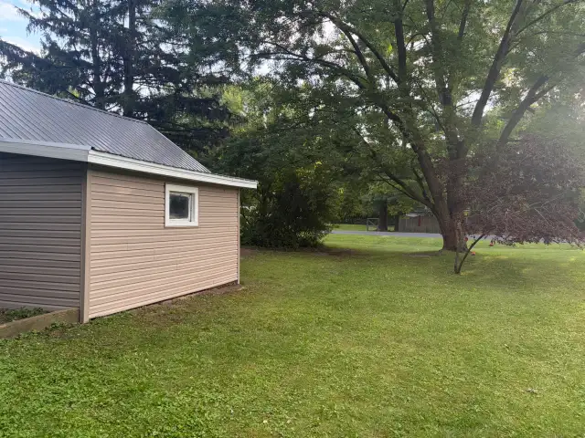 Side view of a detached garage with new tan vinyl siding and gray ribbed metal roof