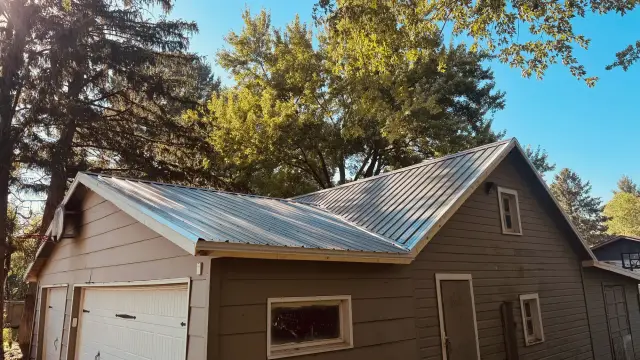 Completed ribbed metal roof on a two-car garage with attached workshop, morning sun on the new panels