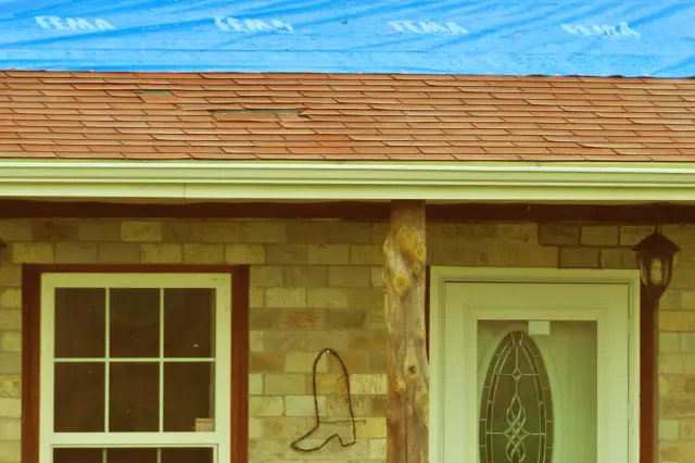 Tornado-damaged home with sections of roof covered in temporary blue emergency tarp